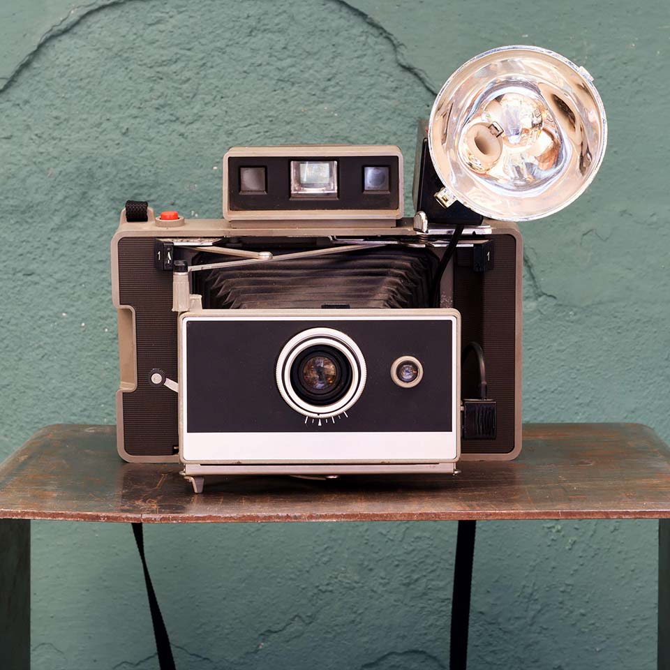 2C97CMM - Old vintage instant camera with bellows and lamp on a small shelf in front of a damaged green textured wall in a photographic concept
