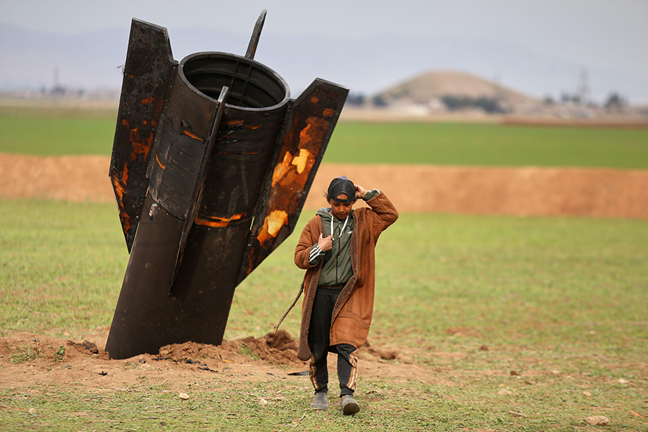 A shepherd boy walks away from an unexploded Iranian projectile that landed in an open field in the outskirts of Qamishli, eastern Syria